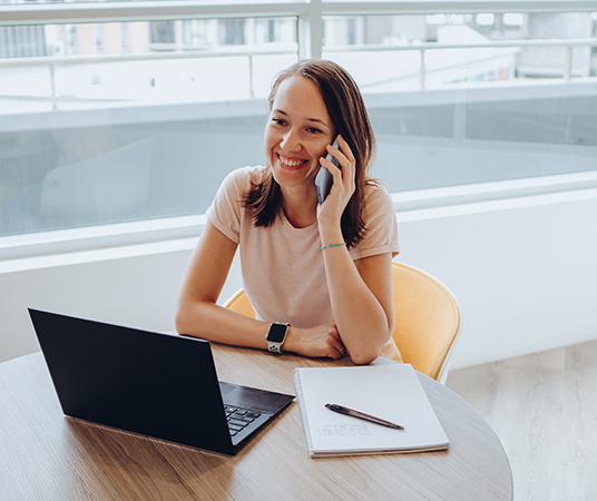 Eine Webdesignerin, die an einem Tisch ein Kundengespräch am Telefon führt.